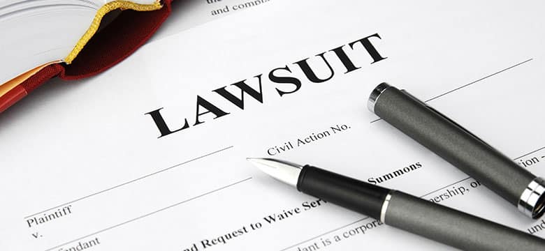 A document titled Lawsuit with a fountain pen and a black pen resting on top, partially visible book with a red ribbon bookmark in the upper left corner.