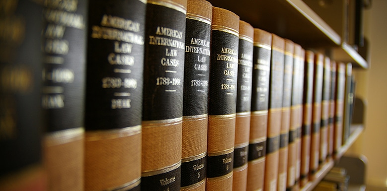 A row of thick legal books with black and gold labels on a library shelf, titled American International Law Cases, neatly aligned in perspective from left to right.