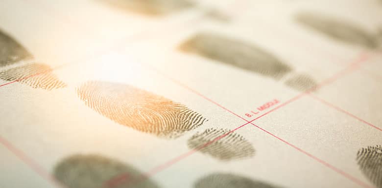 Close-up of black ink fingerprints on a paper fingerprint card, with several fingerprint impressions arranged in rows and columns under soft lighting.