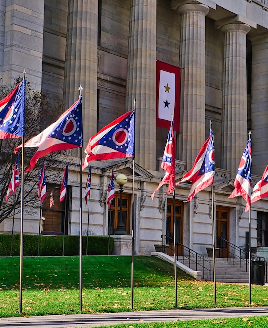 state of Ohio flags aligned with the Ohio statehouse / Capital in downtown Columbus Ohio.