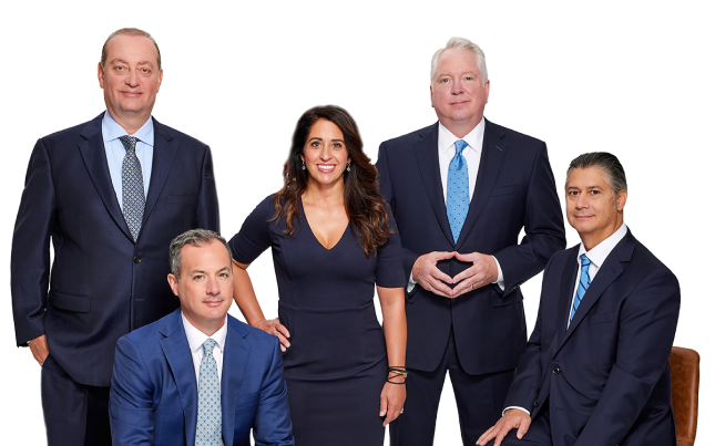 Five business professionals in suits, four men and one woman, pose together against a plain white background. Some are standing, while two men are seated. All are smiling and looking at the camera.