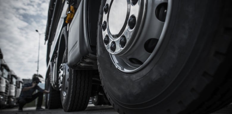 Close-up view of large truck wheels with a person in the background inspecting or working near the truck, under a cloudy sky.