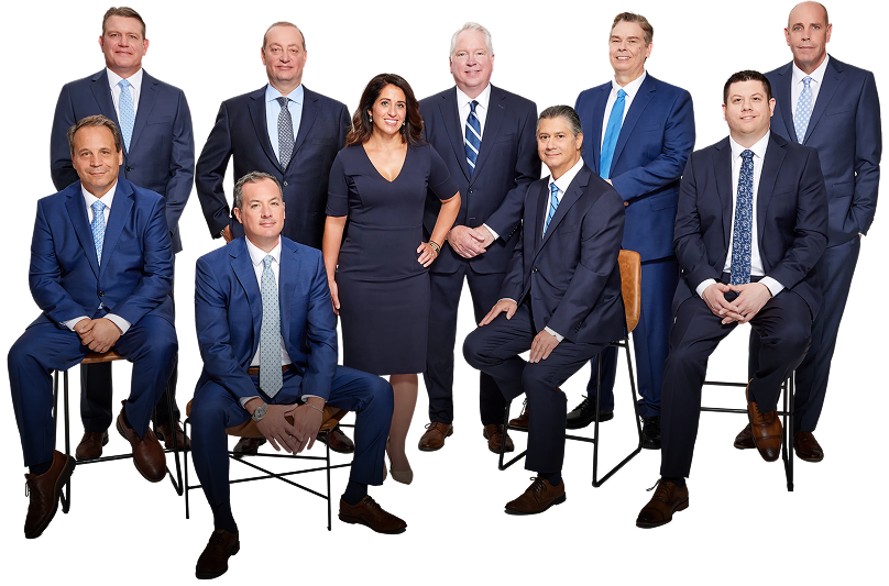 Nine professionally dressed people pose together against a white background; six men are standing, two men and one woman are seated or perched on stools, all wearing business attire and looking at the camera.